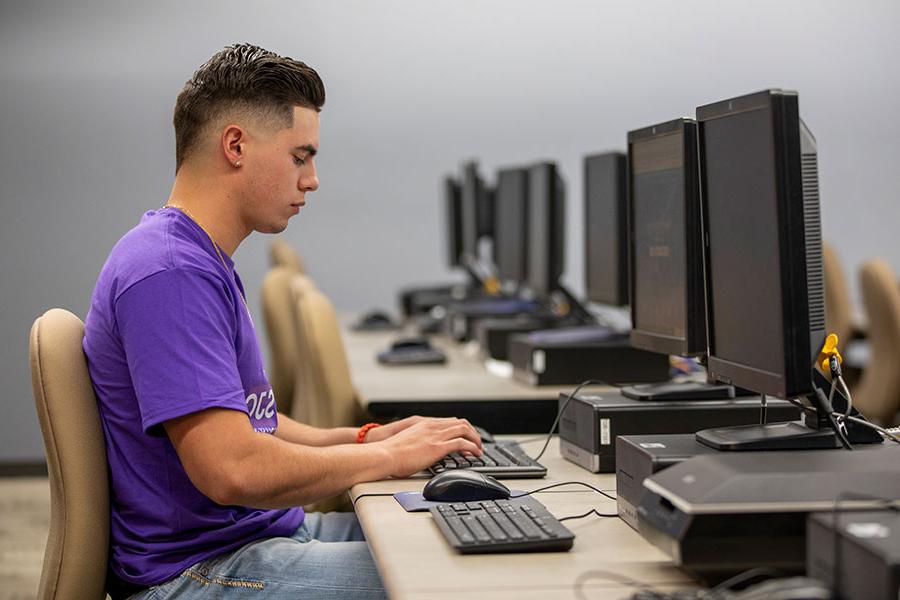 一个穿着紫色衬衫的人坐在电脑前，在键盘上打字