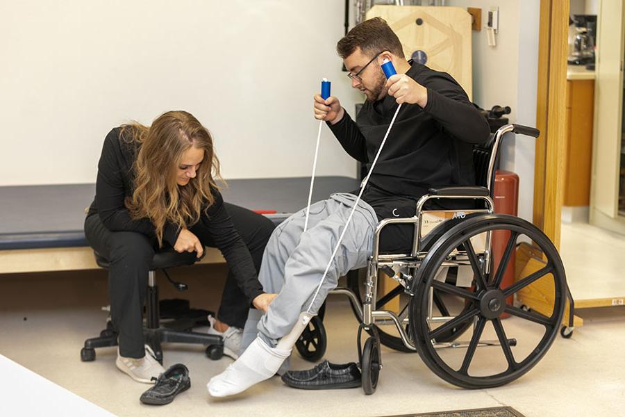 一个学生在评估另一个坐在轮椅上的学生的腿